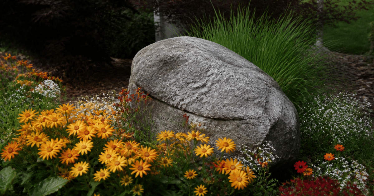 Grand pierre decorative posee dans parterre floral paysage.