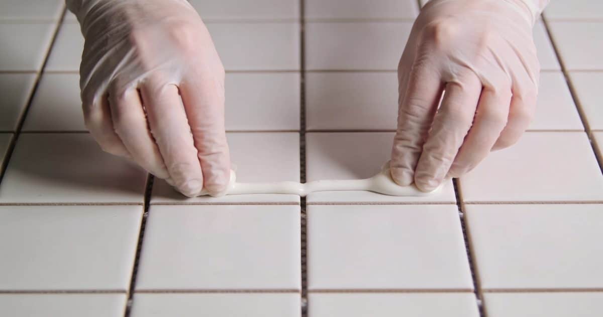 Mains gantees appliquant du coulis blanc entre carreaux.