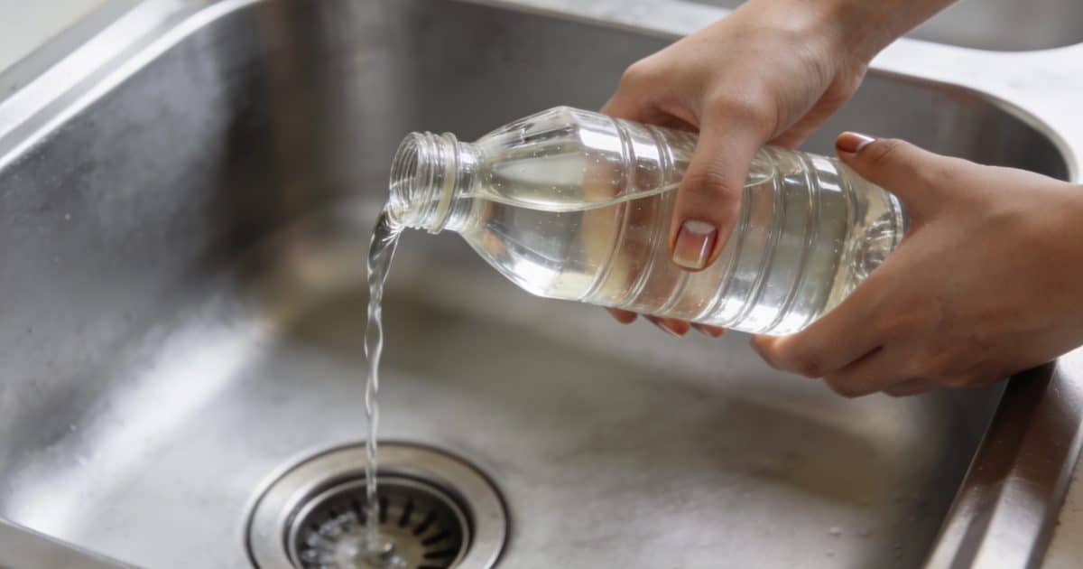 Mains versant vinaigre blanc dans un évier bouché.