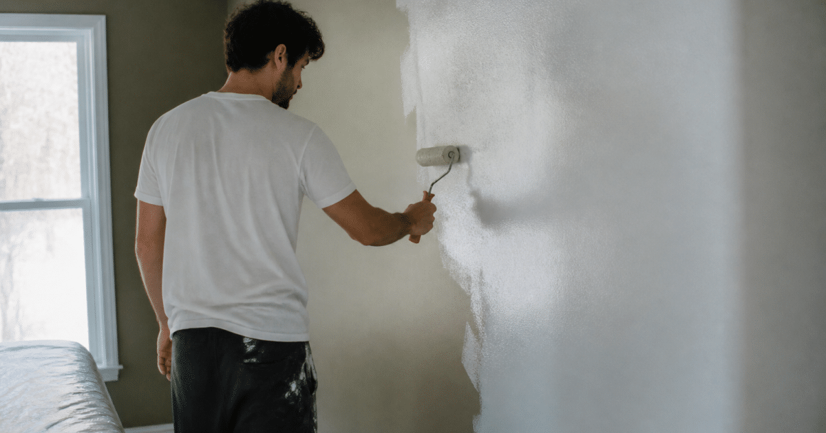 Personne appliquant peinture murale dans une chambre residentielle.