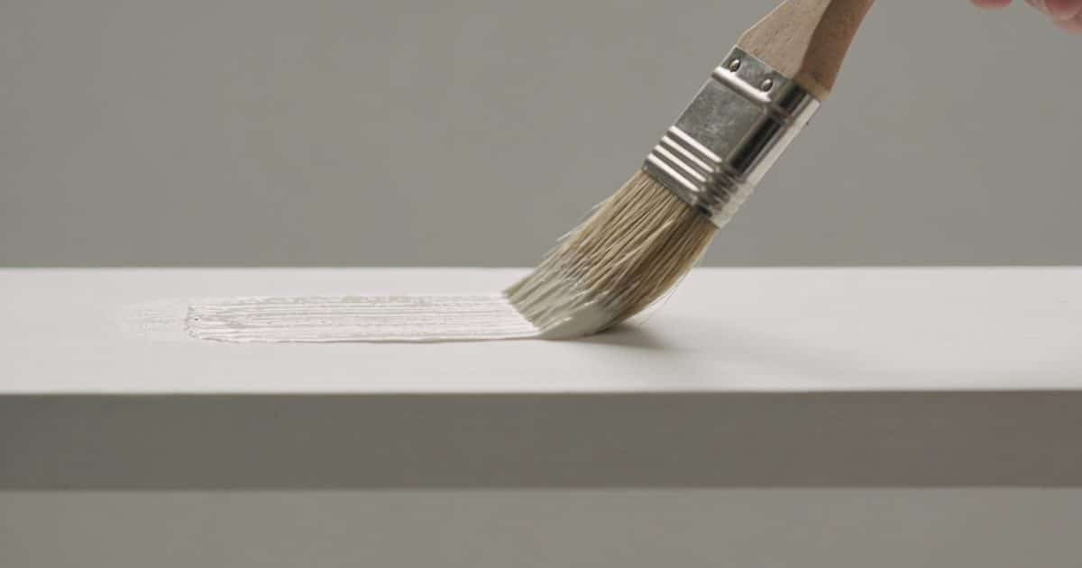 Pinceau appliquant peinture sur surface blanche horizontale.