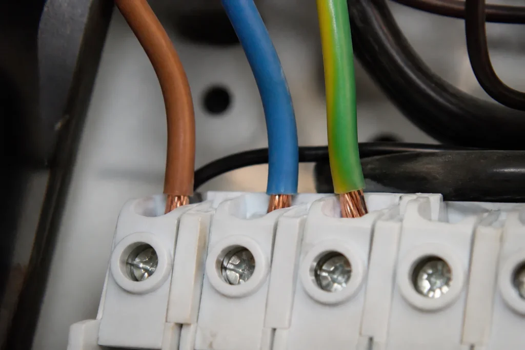 Main gantee serrant cables marron bleu vert sur bornier
