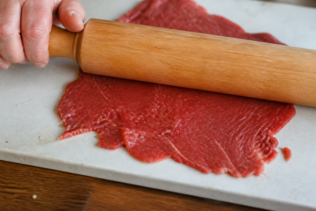 Viande mince aplatie sous rouleau sur plan